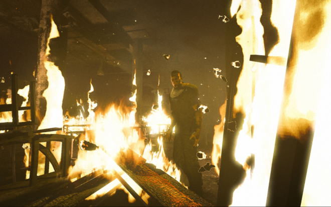 A dark, low-angle shot of the interior scene shows multiple flames engulfing wooden structures and furniture in an abandoned warehouse-like setting.